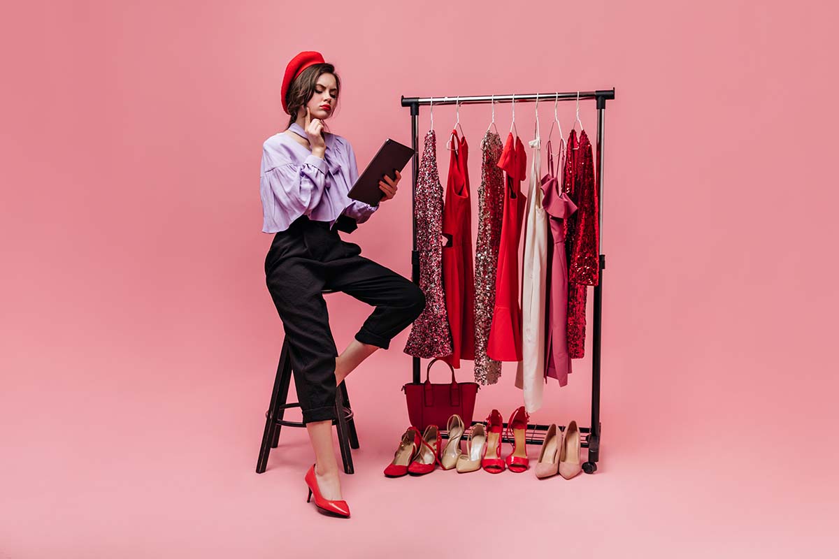 Girl in stylish outfit and red beret sits on chair and thoughtfully reads on pink background with shiny clothes and shoes