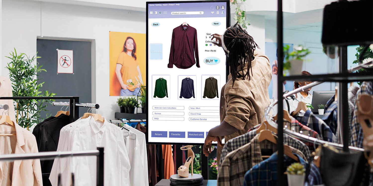 Man uses digital display to view shirts and jackets for sale in luxury retail shop.
