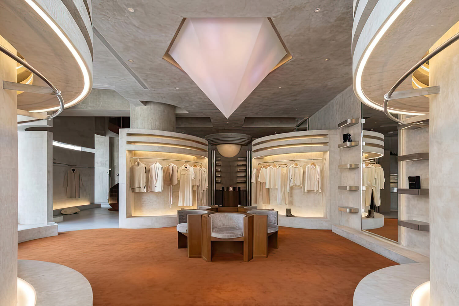 Luxury retail space with chairs in the middle of the room and clothing on display in each of the corners